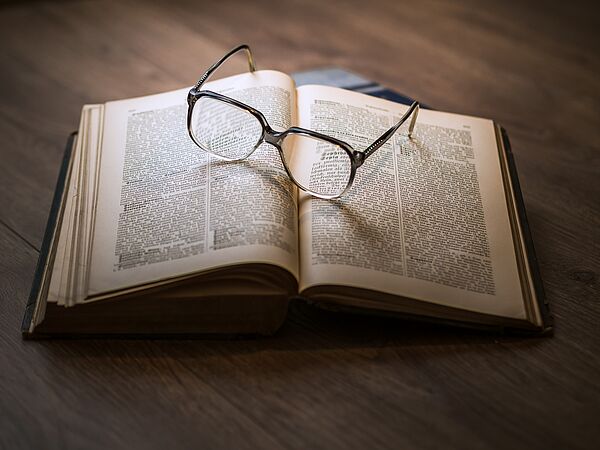 Das Bild zeigt ein Buch mit viel Text auf dem eine Sonnenbrille liegt.